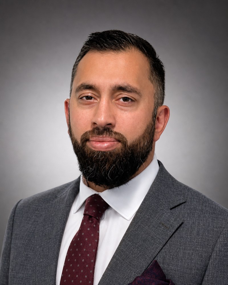 Ali M. Chaudhry, Esq., founder of Chaudhry Law, PLLC, in a charcoal suit with a burgundy tie