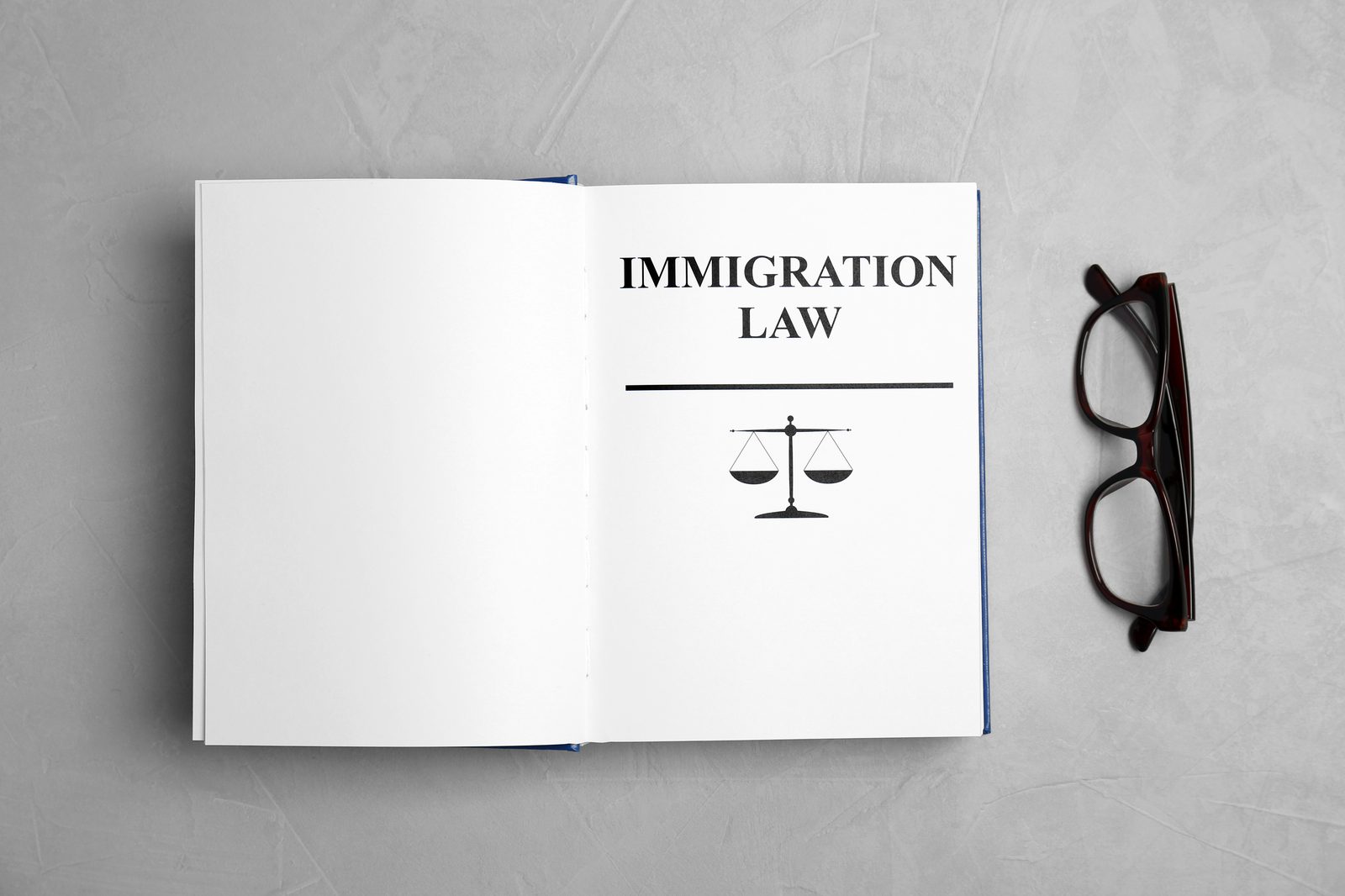 An open Immigration Law book beside reading glasses on a stone surface